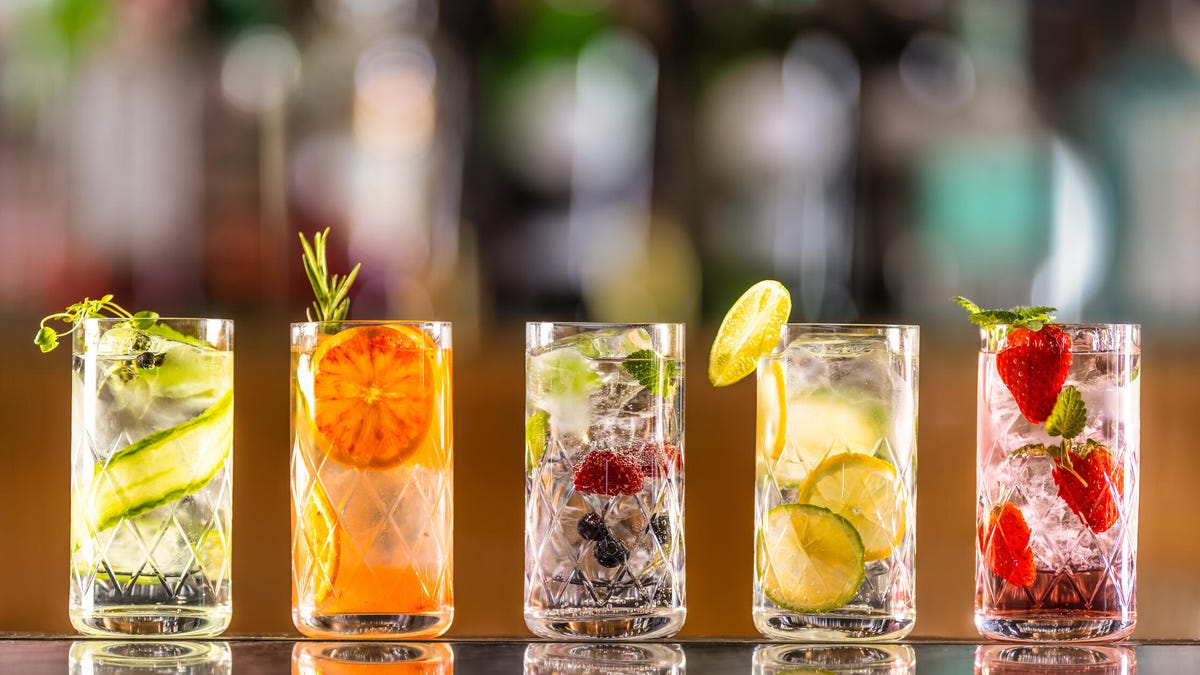 Five glasses with ice, fruit and a fizzy beverage.