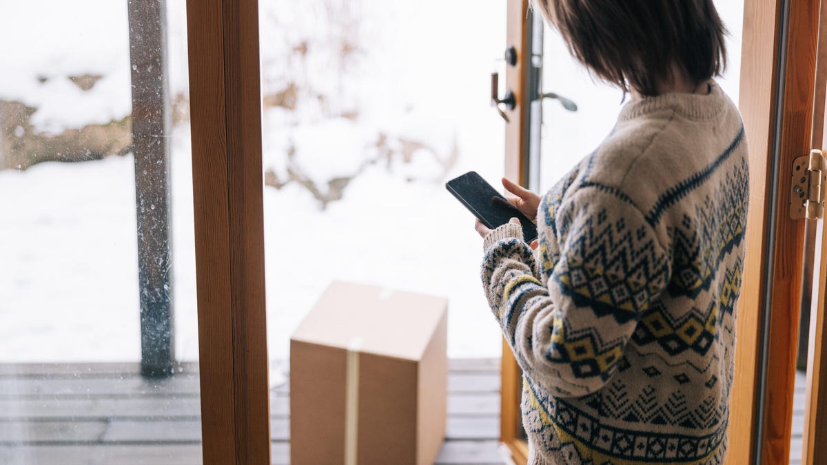 woman using a smartphone while receiving a package at home during winter time.