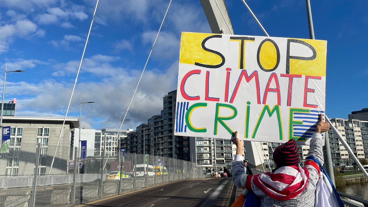 A protester outside of the COP26 Blue Zone holding a sign that says "Stop Climate Crime"