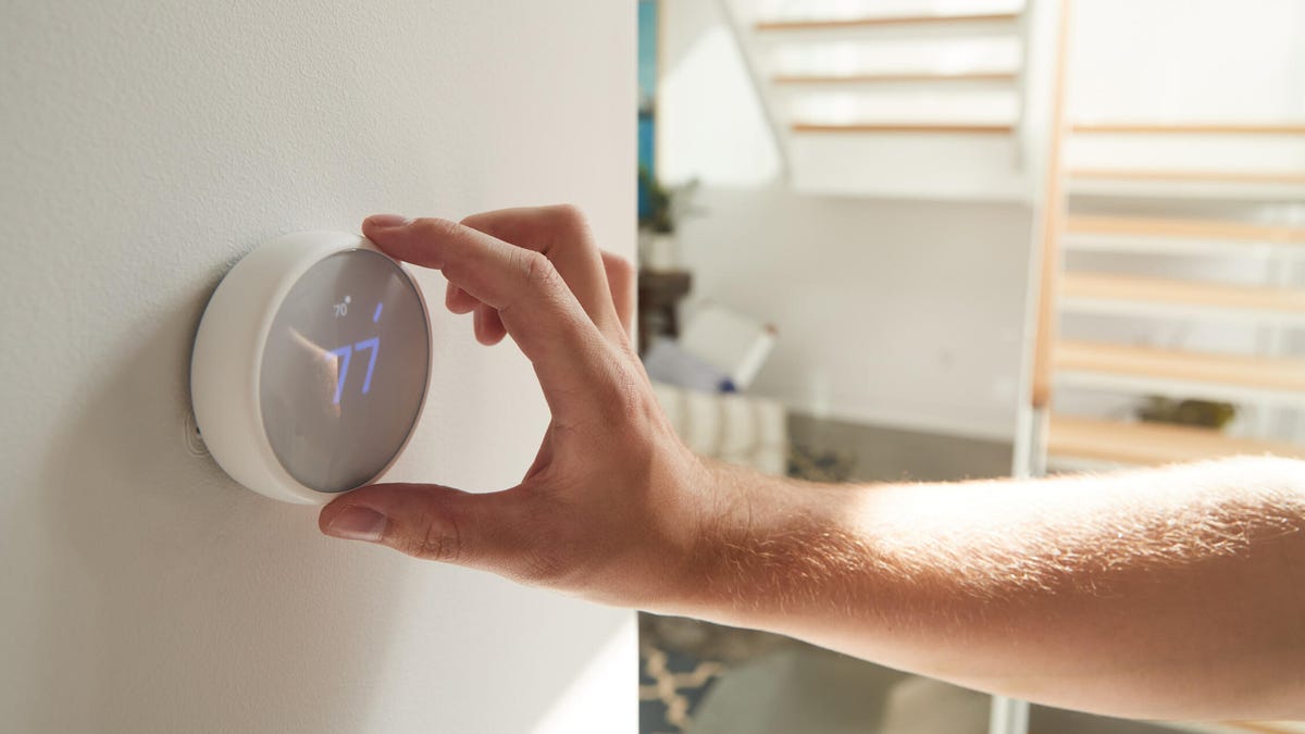 A hand in a sunny room reaches out to change a round smart thermostat.