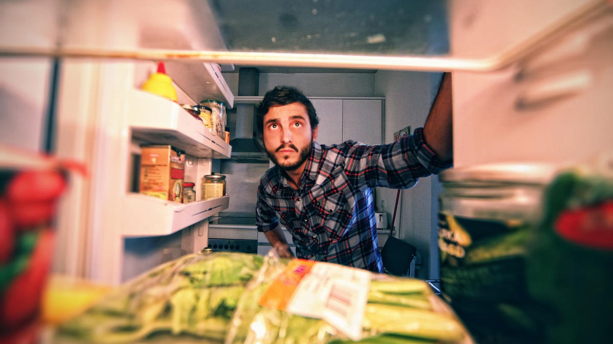 A view from inside a refrigerator as a man in plaid peers inside.