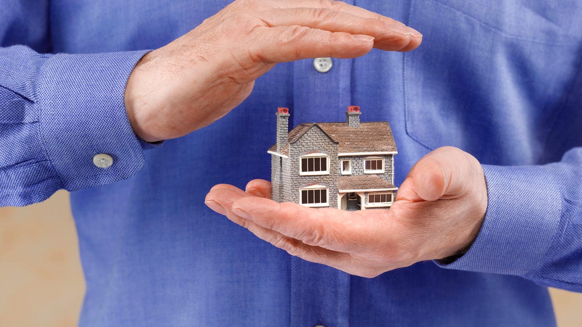 A man in blue holds hands over a tiny house model.