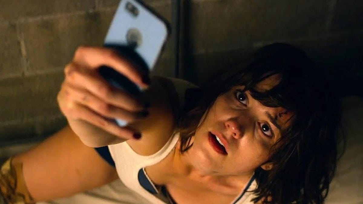 Mary Elizabeth Winstead wears a sleeveless white shirt and looks at her phone.