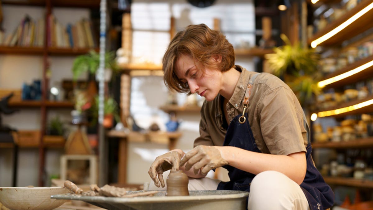 Woman sitting in front of a pottery wheel, molding clay.