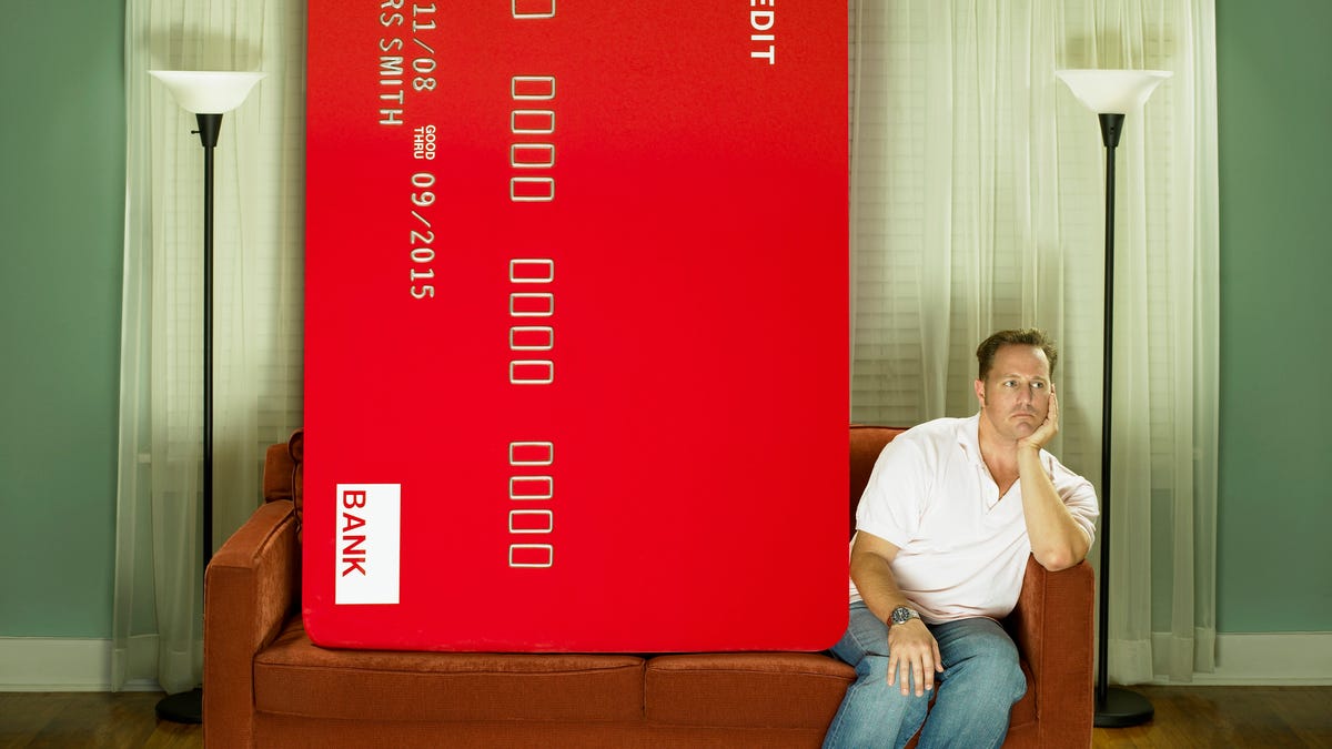 Giant credit card looming over man on couch