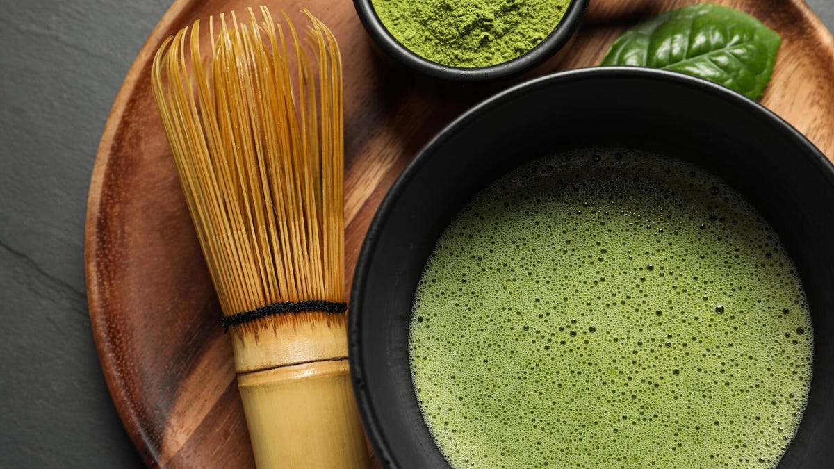 Cup of fresh matcha tea, bamboo whisk and green powder on black table, top view