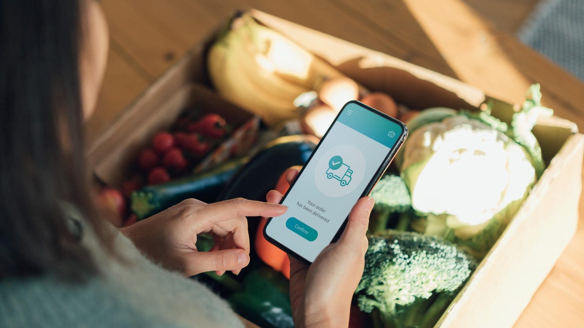 person holding phone over delivery of groceries