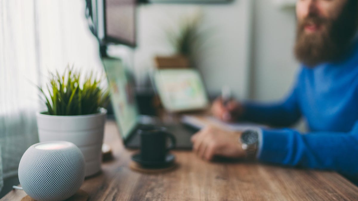 Man sits at a wood table behind a HomePod.