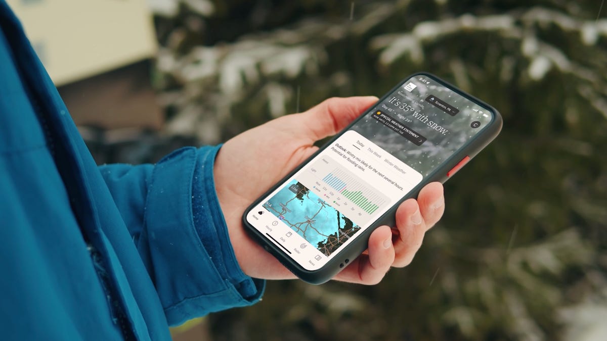 A person holding a phone with the Weather Channel app on the screen