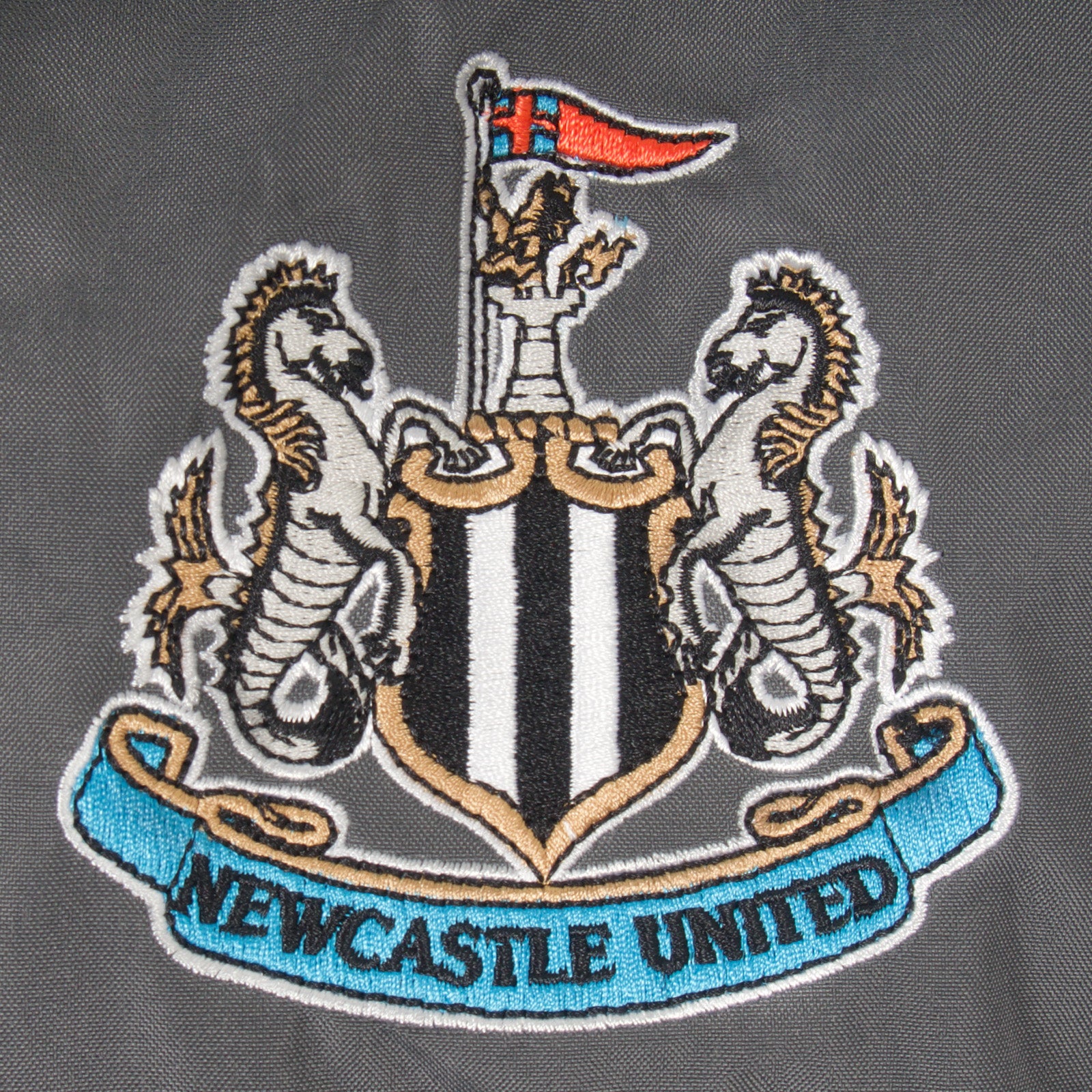 Newcastle Utd kids shower jacket in black & grey with club crest to chest.